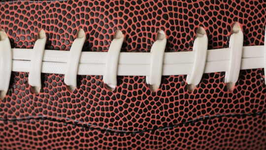美式橄榄球棕色皮革和白色鞋带的特写。