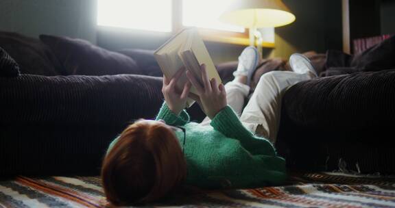 女孩双腿挂在沙发上读书