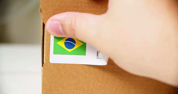 双手在装有产品的运输纸箱上贴上MADE IN BRAZIL标志标签。特写镜头wi