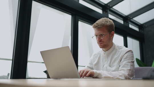 英俊的男人白天在现代办公室用笔记本电脑工作，穿白衬衫的人在冲浪