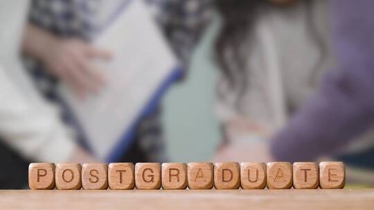 木制字母立方体或骰子拼写研究生与学生在背景中会面的教育理念