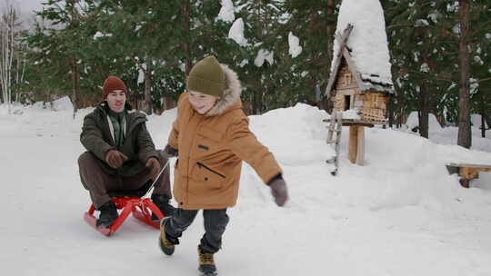 在雪地森林里，快乐的小男孩拉着雪橇上笑着