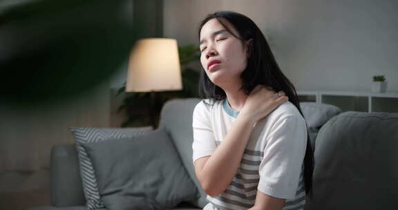 年轻女子颈部疼痛，肩膀坐在家里的沙发上。