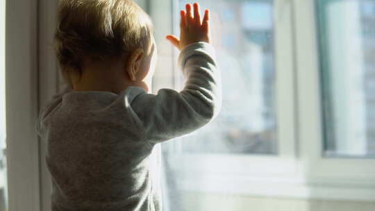 微笑的婴儿站在家里靠近窗户的白色房间里