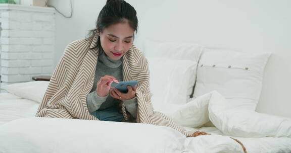 年轻亚洲女孩在床上玩手机在社交媒体发消息