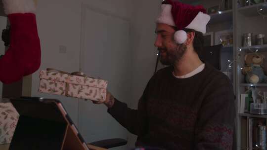 一名男子戴着圣诞帽在视频电话中展示圣诞礼物