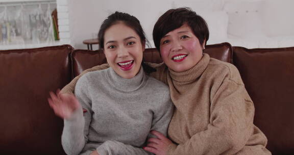 女儿和母亲微笑坐在沙发上看镜头视频聊天