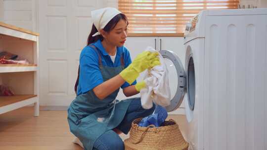 亚洲年轻女清洁工把脏衣服放在家里的洗衣机
