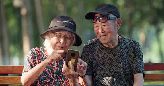 老年夫妇在公园长椅上看手机聊天