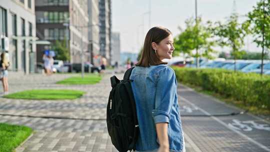 快乐的年轻女子背着背包走在现代城市的街道