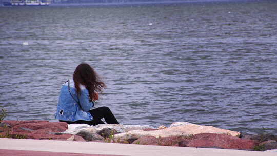 年轻的女孩坐在海边石头上