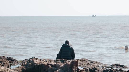 老人坐在海边看向远方的大海船只