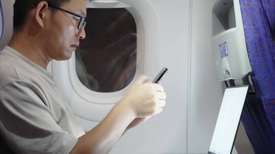男子在飞机上使用笔记本电脑和手机