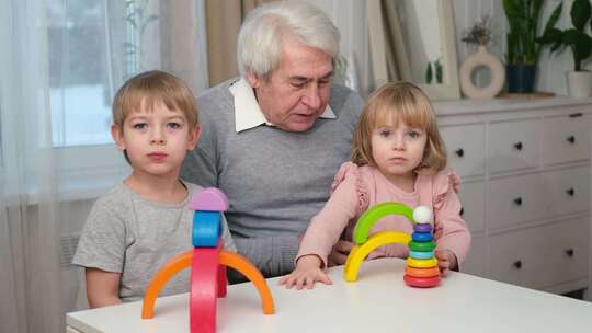 爷爷玩玩具与孙子和小孙女室内老人爷爷一起