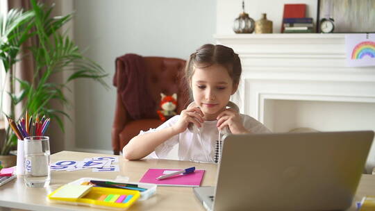 现代在线教育。Spbd Girl戴上耳机参加远程课程。年轻的女学生坐在桌子旁，家里的房间里有笔记本电脑和学习用品