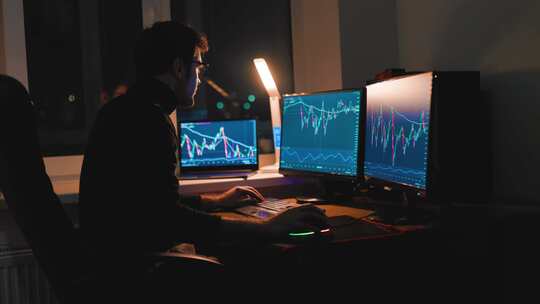 夜晚一男子在电脑前研究股票市场K线图