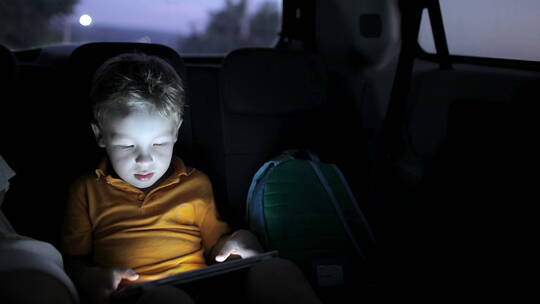 夜里男孩在车上玩平板
