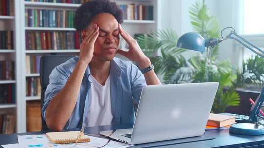 年轻疲惫的非裔美国人头痛坐在办公室的桌子旁视频素材模板下载