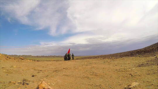 沙漠戈壁中举红旗行走的边防战士队 前拍摄