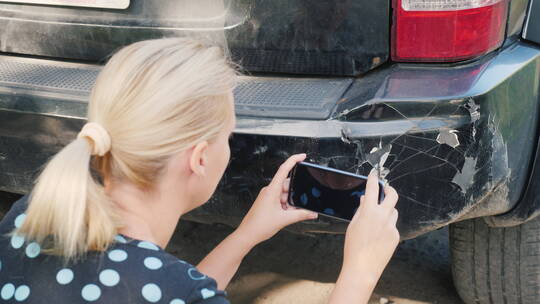 一名妇女拍摄一辆损坏的汽车保险杠