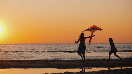 日落时分妈妈和女儿在海边快乐的放风筝