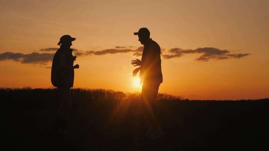 两个农民在太阳落下的天空下的田野剪影中快