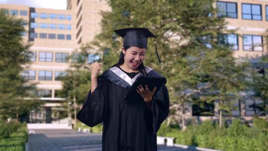 学生毕业生看着平板电脑，然后在大学门前庆