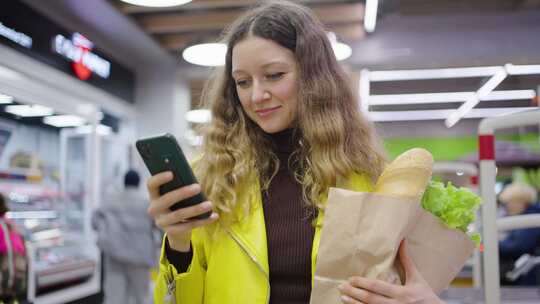 年轻女子在杂货店使用智能手机，纸袋里装着