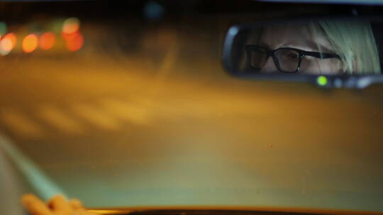 戴眼镜的女人开车穿过夜城