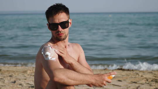 海滩上戴太阳镜的高加索男子为皮肤涂抹防晒视频素材模板下载