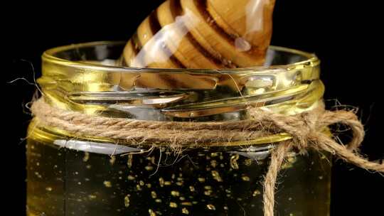 蜂蜜从勺子纺锤上流下来，进入一个黑色背景上有蜂蜜的罐子。视频素材模板下载