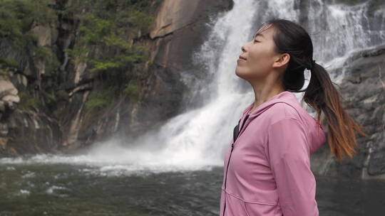 亚洲中国人女性在瀑布下张开双臂拥抱自然