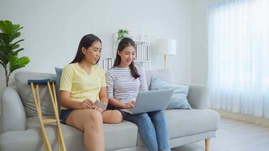 亚洲女性截肢者与朋友在客厅使用笔记本电脑。