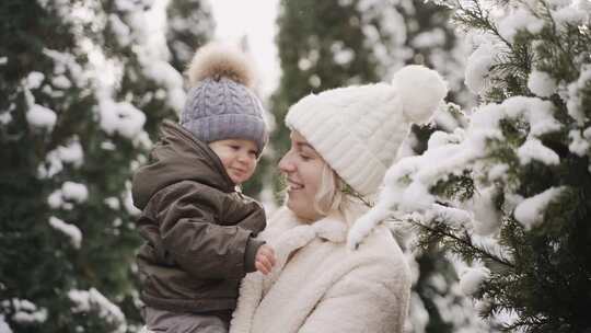 一个女人抱着一个婴儿在白雪覆盖的松树旁