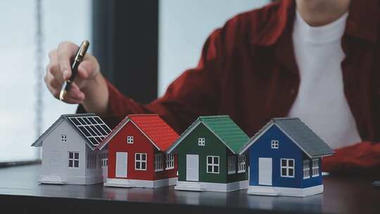 手持钢笔指向彩色房屋模型
