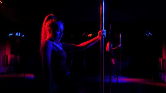 一个性感女孩在明亮的聚光灯下靠近杆子的剪
