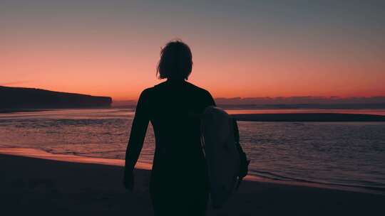 日落时分，女人带着冲浪板走进大海