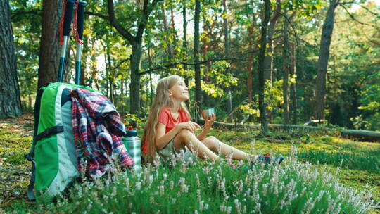 女孩坐在在森林草地上喝水