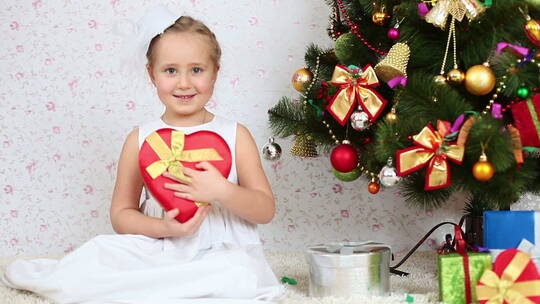 女孩抱着礼物坐在圣诞树旁视频素材模板下载