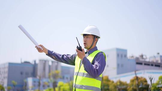 年轻工程技术人员手拿对讲机和图纸现场指挥