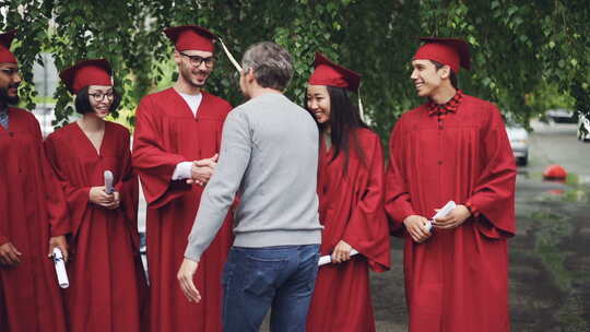 骄傲的大学老师拥抱他的学生并握手，毕业生