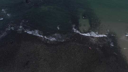 上帝视角下黑沙滩上海浪拍打着黑礁石视频素材模板下载