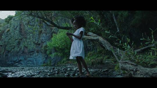 非洲女孩在河边站着抚摩石头