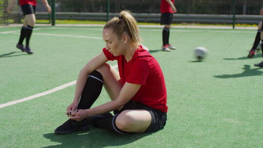 女足球运动员坐在操场上系鞋带