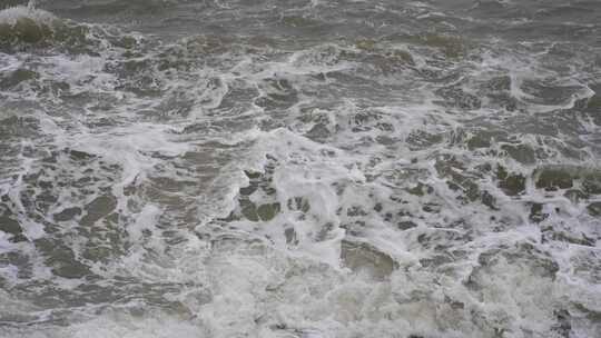 海浪拍打岩石浑浊海水冲刷礁石浪花阴天大海