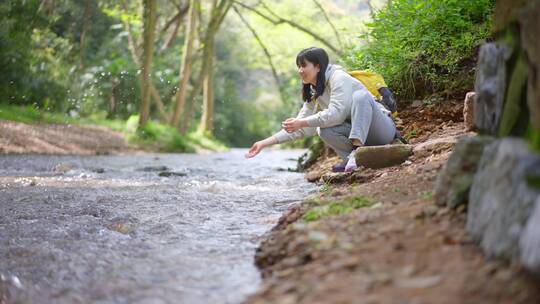 春天年轻女孩郊游公园蹲在小溪边洗手玩水