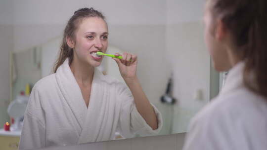 年轻苗条黑发白人妇女用牙刷刷牙的镜子里的视频素材模板下载