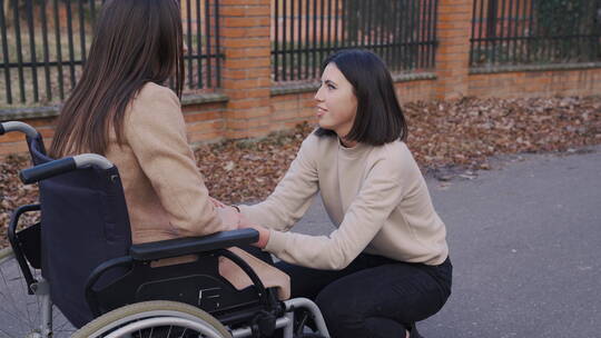 女人蹲着和坐在轮椅上的朋友聊天