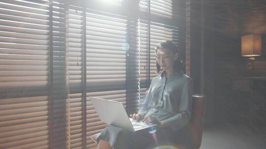 女人坐在百叶窗前操作电脑视频素材模板下载