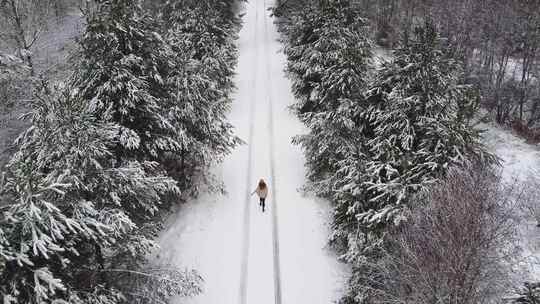 航拍在大雪纷飞的道路上蹦跑的女生